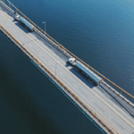 Aerial view of two tanker trucks driving across a bridge over blue water.