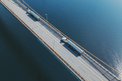 Aerial view of two tanker trucks driving across a bridge over blue water.