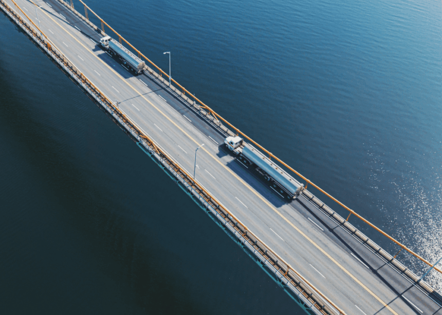 Aerial view of two tanker trucks driving across a bridge over blue water.