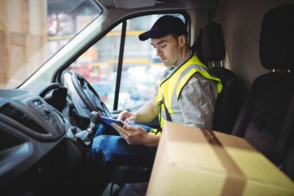 A delivery driver sits in a van, reviewing information on a digital tablet.