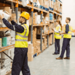 Warehouse workers in high-visibility vests organize and scan inventory on shelves.