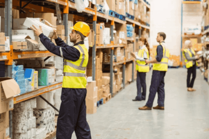 Warehouse workers in high-visibility vests organize and scan inventory on shelves.