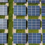 Aerial view of solar panel arrays arranged in rows over a grassy field.
