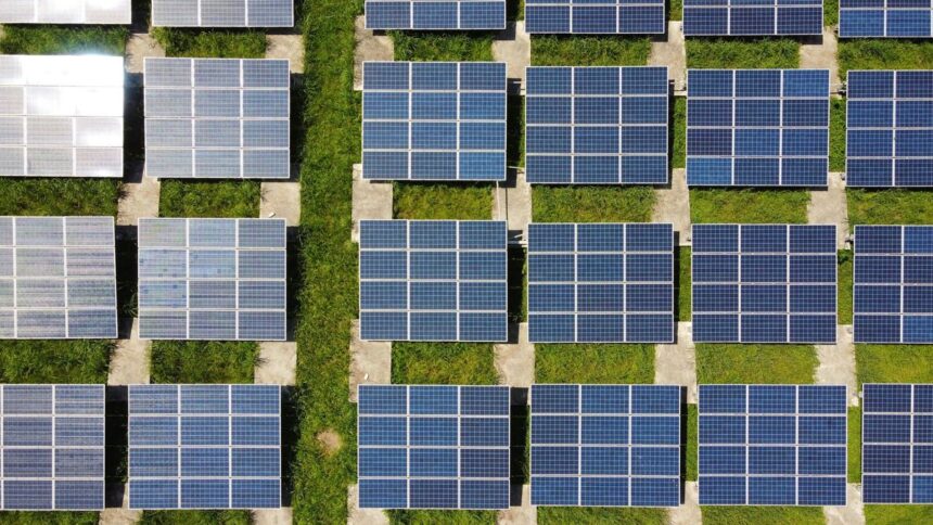Aerial view of solar panel arrays arranged in rows over a grassy field.