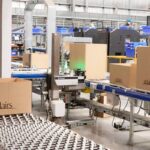 Warehouse staff working with cardboard boxes on automated conveyor belts in a distribution center.