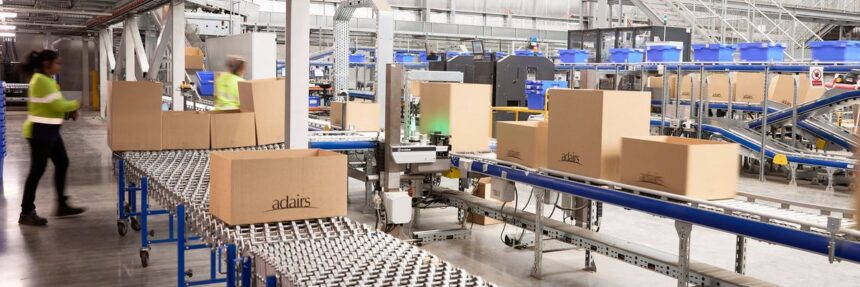 Warehouse staff working with cardboard boxes on automated conveyor belts in a distribution center.