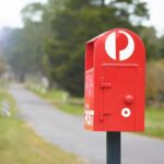 A bright red Australia Post mailbox standing beside a rural paved path.