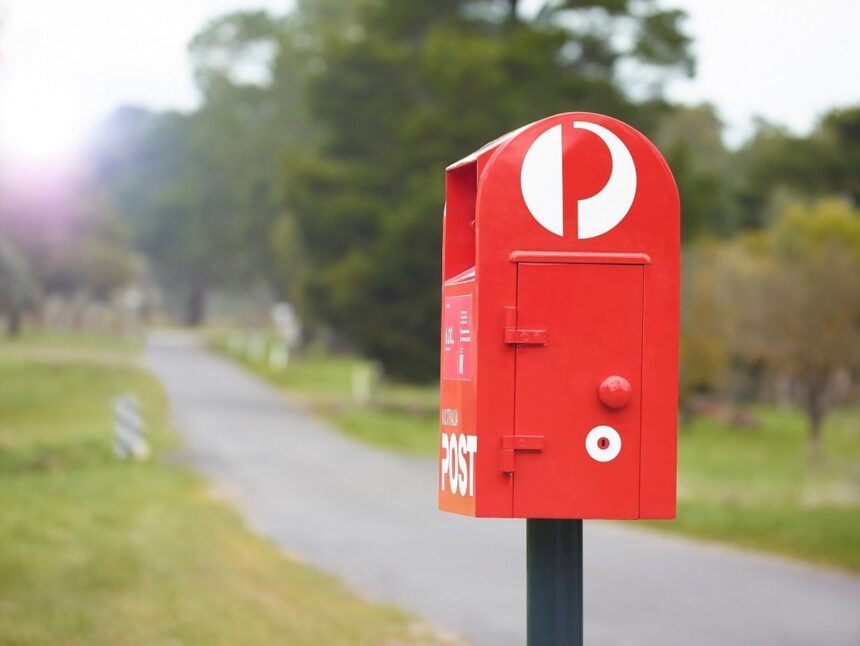 A bright red Australia Post mailbox standing beside a rural paved path.