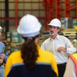 A manager leads a safety meeting with a team of industrial workers in a warehouse.