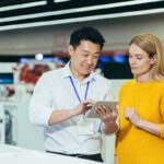 A male store clerk shows a tablet to a female customer in an appliance store.