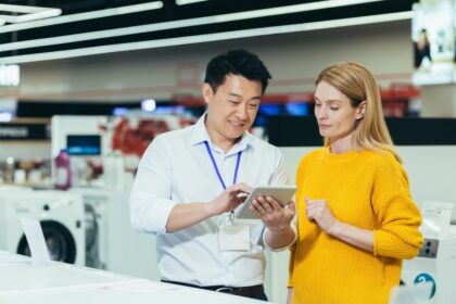 A male store clerk shows a tablet to a female customer in an appliance store.