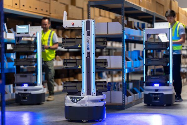 Autonomous mobile robots with shelving units move through a warehouse alongside workers.