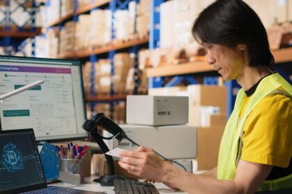 Warehouse worker scanning a package label in front of computer screens with tracking software.