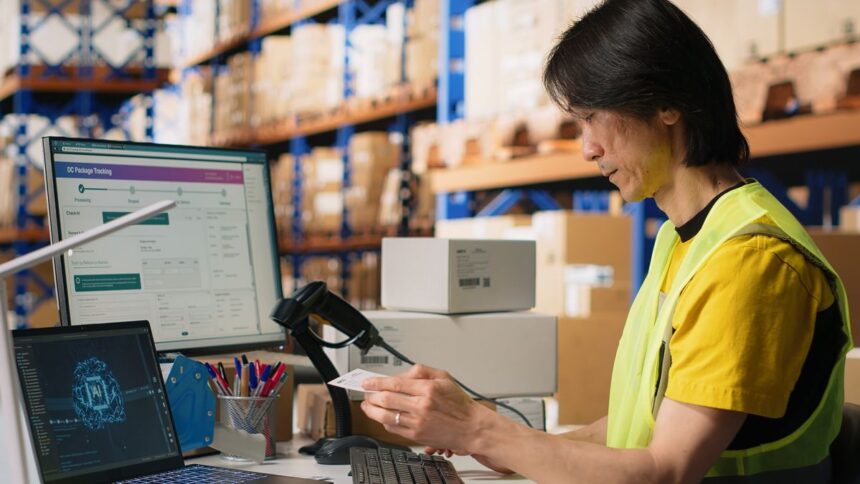 Warehouse worker scanning a package label in front of computer screens with tracking software.