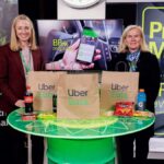 Two women standing behind a table with Uber Eats bags and snacks at a booth.
