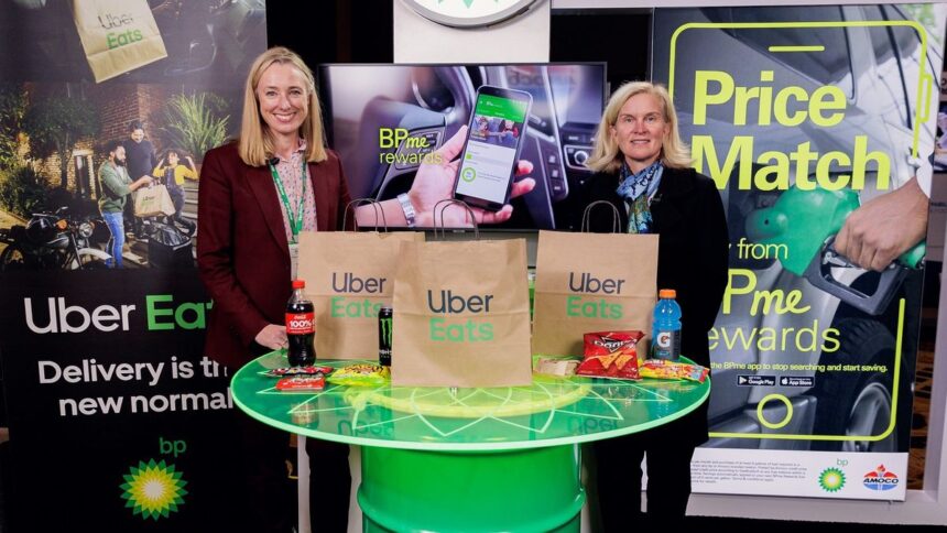 Two women standing behind a table with Uber Eats bags and snacks at a booth.