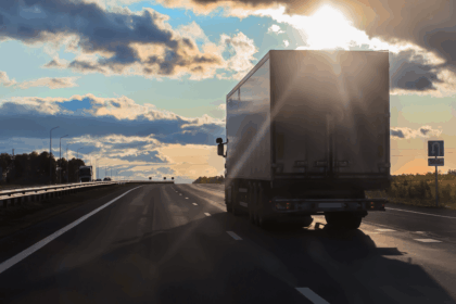 Semi-truck driving down a highway toward the setting sun.
