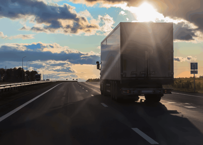 Semi-truck driving down a highway toward the setting sun.