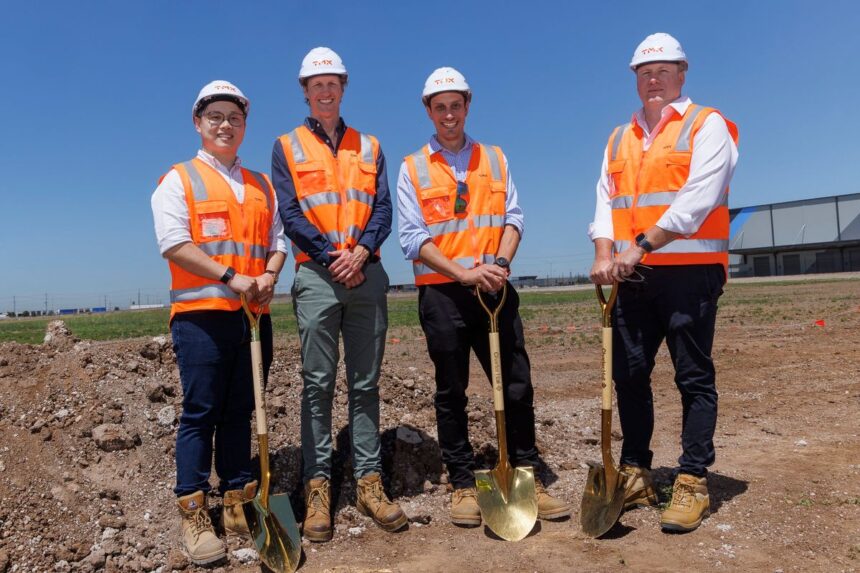 Four men in hard hats and high-visibility vests hold gold shovels at a construction site.