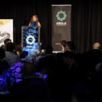 A woman speaking at a podium at the ASCLA awards ceremony before an audience.
