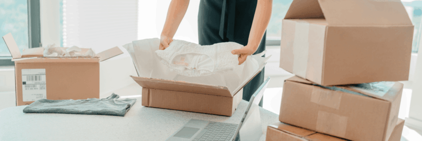 A person packing a white garment into a cardboard shipping box.