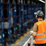 Warehouse worker in a high-visibility vest using a tablet in a logistics center.