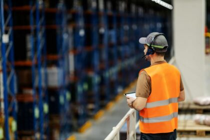 Warehouse worker in a high-visibility vest using a tablet in a logistics center.