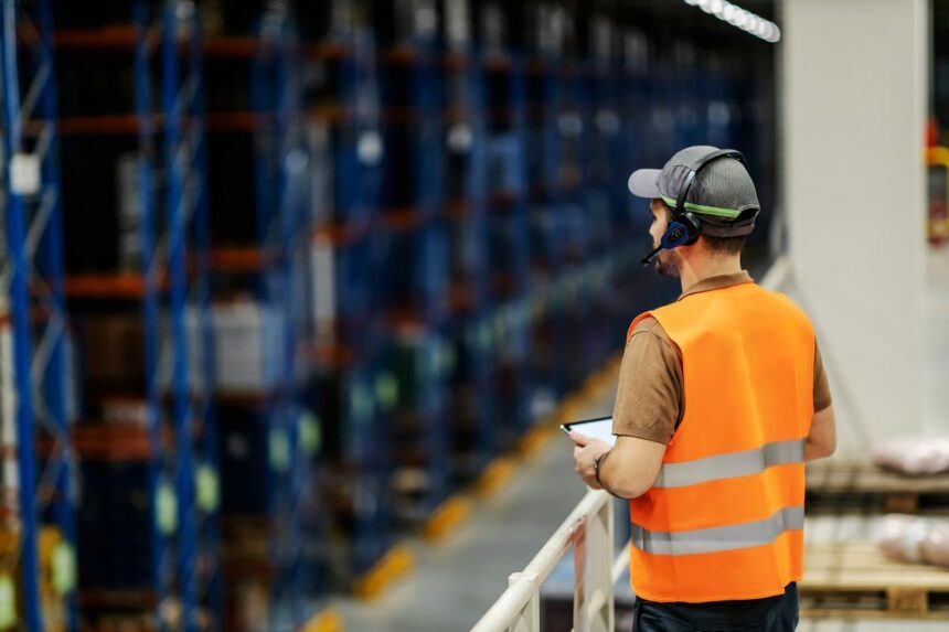 Warehouse worker in a high-visibility vest using a tablet in a logistics center.