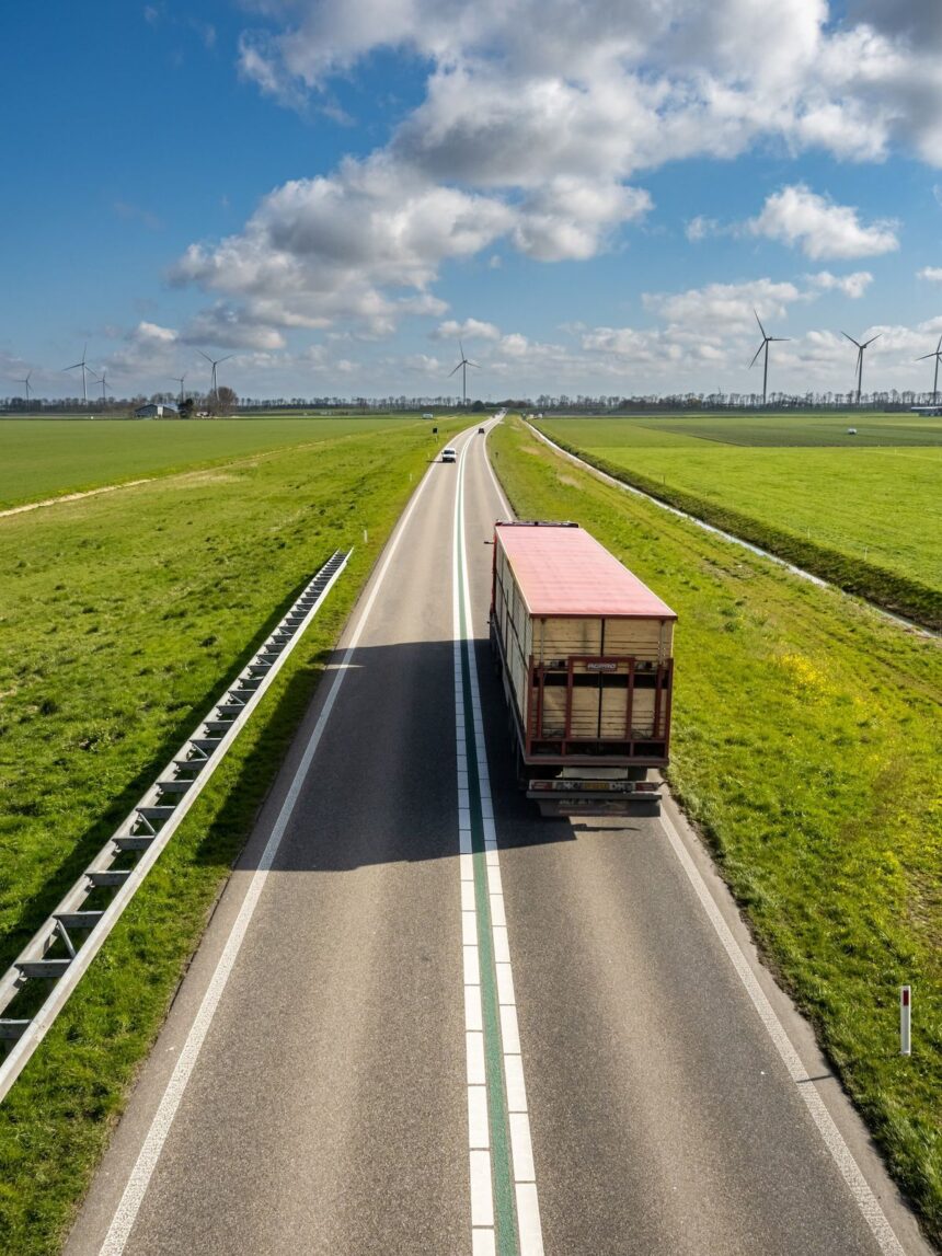 A truck drives on a country road flanked by green fields and wind turbines.