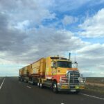 A yellow Kalari road train truck driving on a long, straight desert highway.