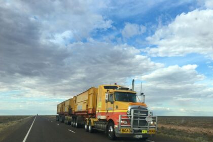 A yellow Kalari road train truck driving on a long, straight desert highway.