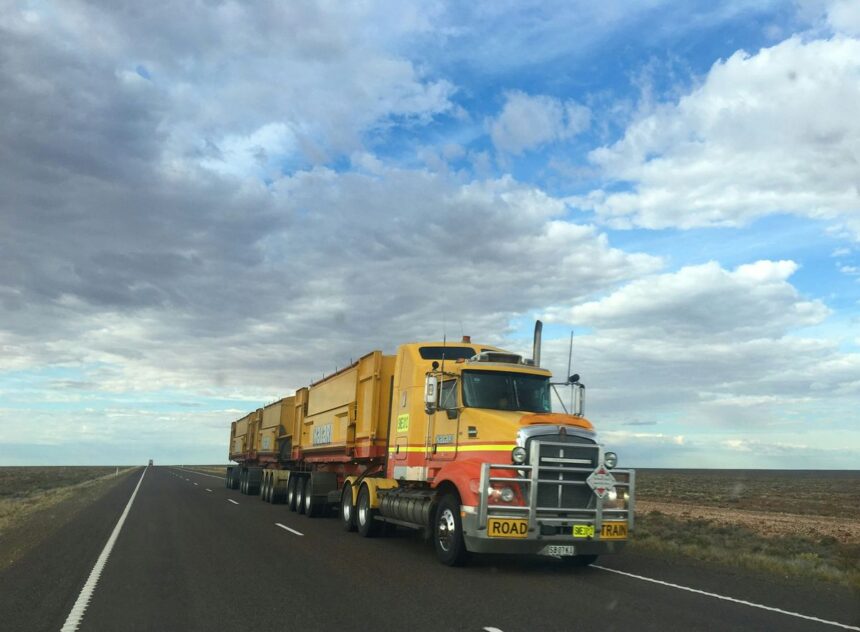 A yellow Kalari road train truck driving on a long, straight desert highway.