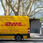 A yellow DHL delivery van parked on a street with a driver standing nearby.