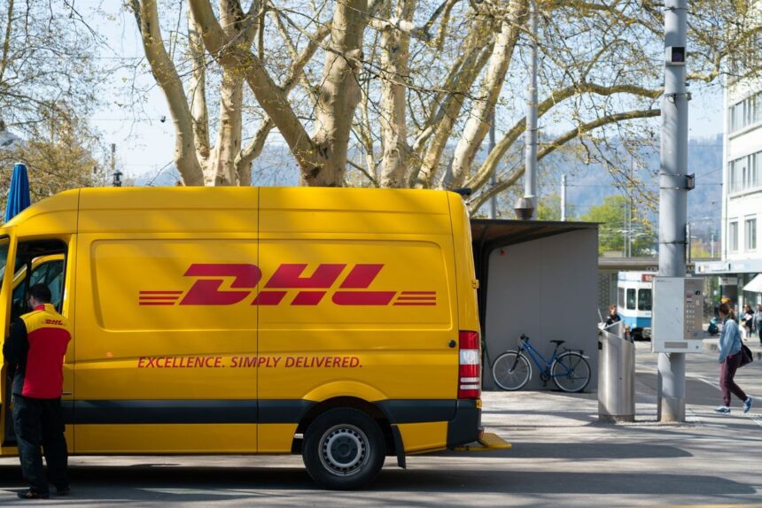 A yellow DHL delivery van parked on a street with a driver standing nearby.