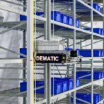 An automated Dematic storage and retrieval machine moving a plastic bin in warehouse racking.
