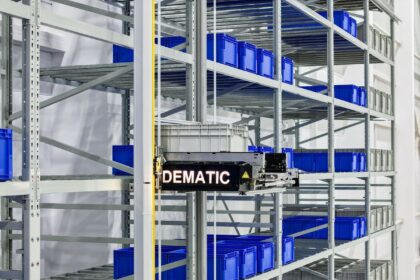 An automated Dematic storage and retrieval machine moving a plastic bin in warehouse racking.