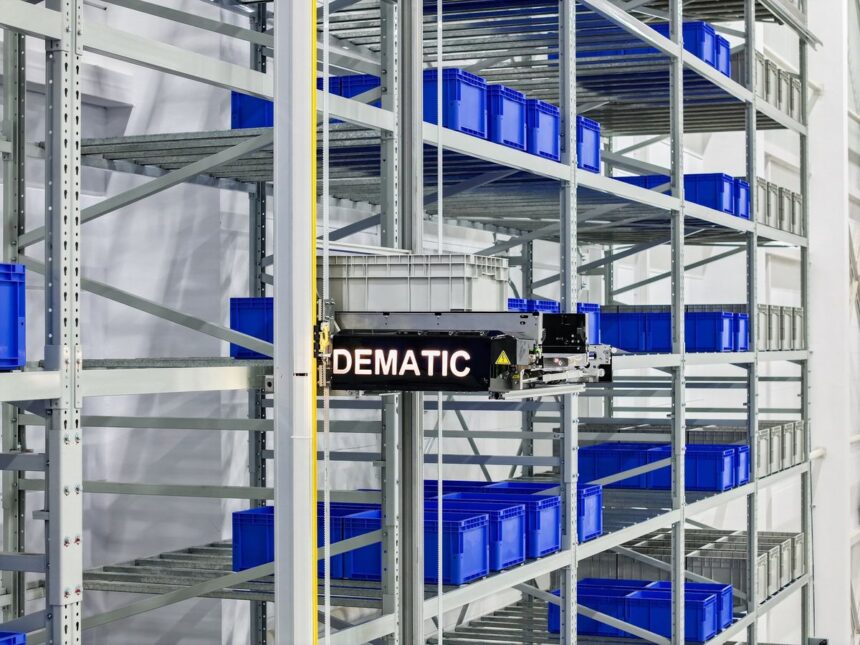 An automated Dematic storage and retrieval machine moving a plastic bin in warehouse racking.