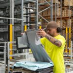 Worker in a high-visibility yellow shirt folding gray t-shirts in a warehouse.