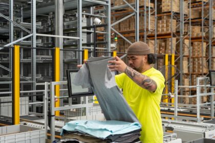 Worker in a high-visibility yellow shirt folding gray t-shirts in a warehouse.
