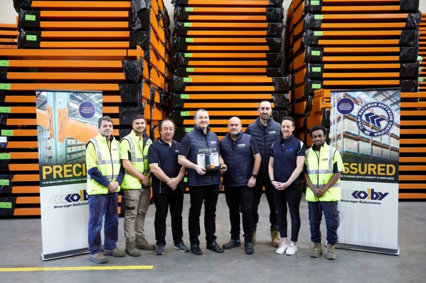 A diverse team stands in a warehouse holding a Distributor of the Year trophy.
