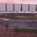 Aerial view of a large modern warehouse building with a parking lot at sunset.