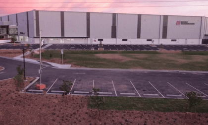 Aerial view of a large modern warehouse building with a parking lot at sunset.