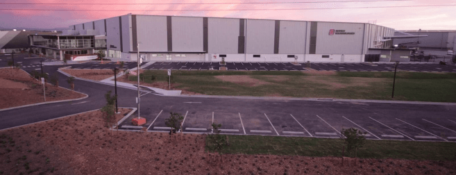 Aerial view of a large modern warehouse building with a parking lot at sunset.