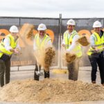 Four men in hard hats and vests performing a ceremonial ground-breaking at a construction site.