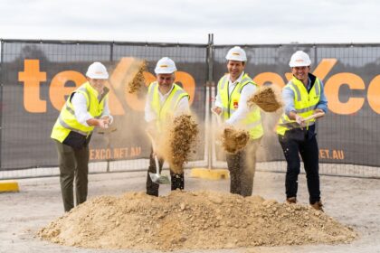 Four men in hard hats and vests performing a ceremonial ground-breaking at a construction site.