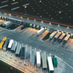 Aerial view of a large logistics warehouse loading dock with parked semi-trailers at night.