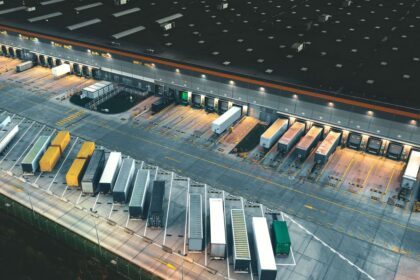 Aerial view of a large logistics warehouse loading dock with parked semi-trailers at night.