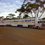 A Direct Freight Express B-double truck parked on a dirt road near trees.