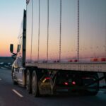 A semi-truck driving on a highway during a colorful sunset.