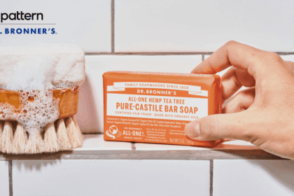 A hand holding a bar of Dr. Bronner's soap next to a soapy brush.